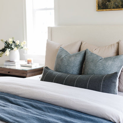 Bed styled with gray and cream decorative pillows, white bedding, and blue textured throw blanket.