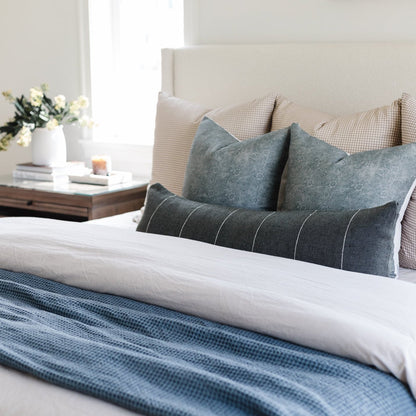 Framed art print displayed above a bed with gray and striped pillows and blue bedding.