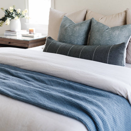 Storm blue waffle-textured blanket draped across a bed with white bedding and gray pillows.