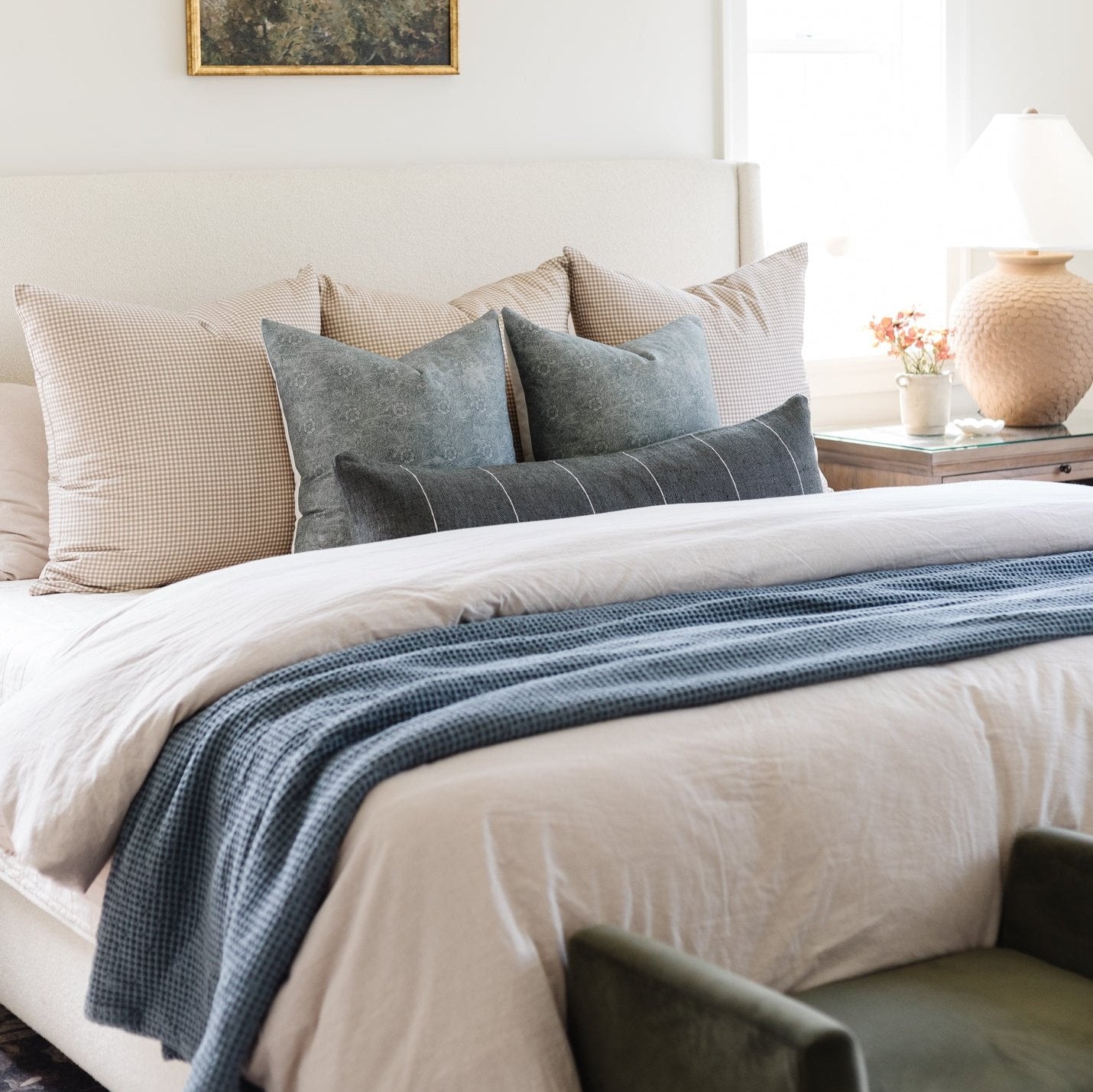 Framed artwork featuring a small bird perched among moss-toned foliage displayed above a bedroom bed.