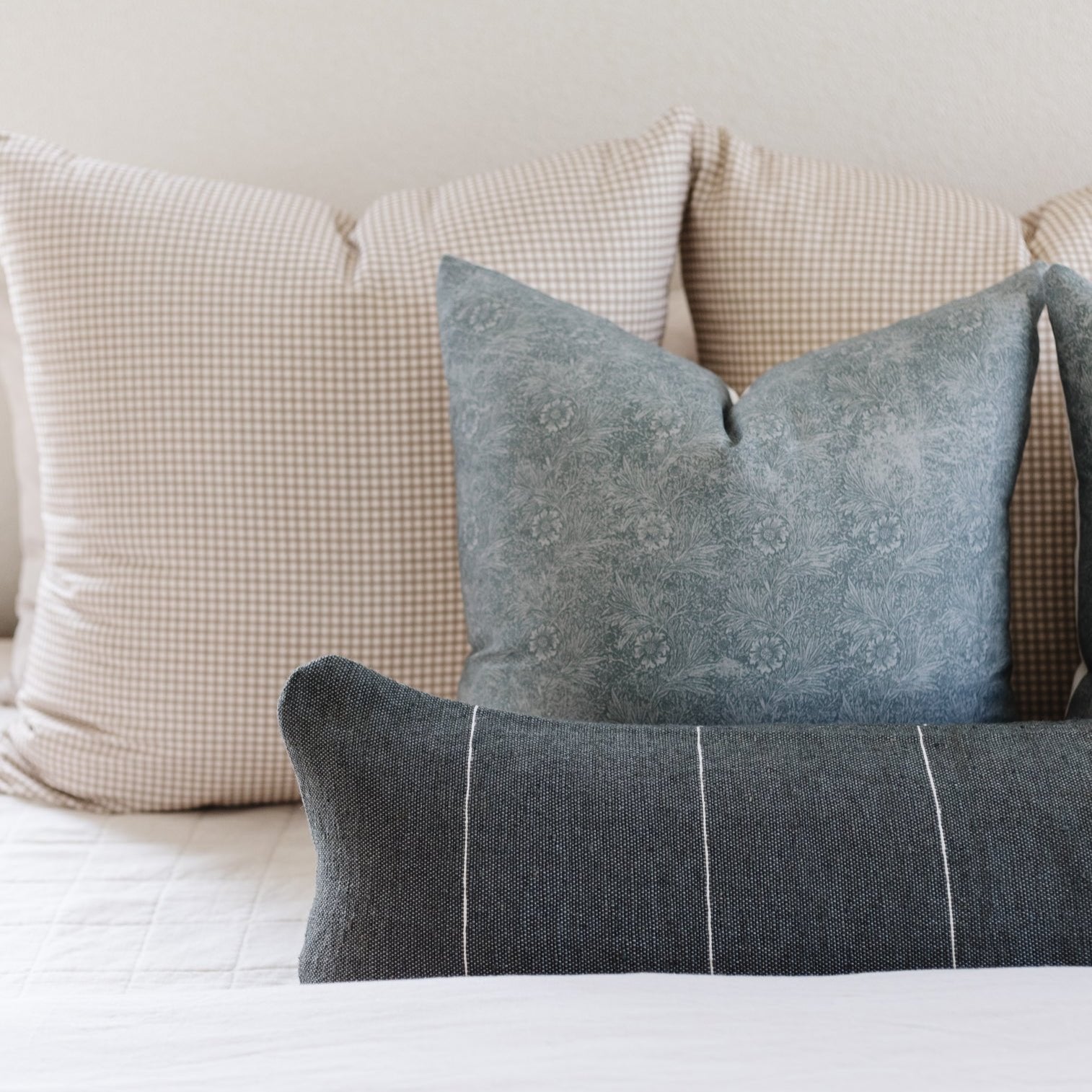 Three decorative pillows: beige gingham, blue damask, and charcoal with white stripes.