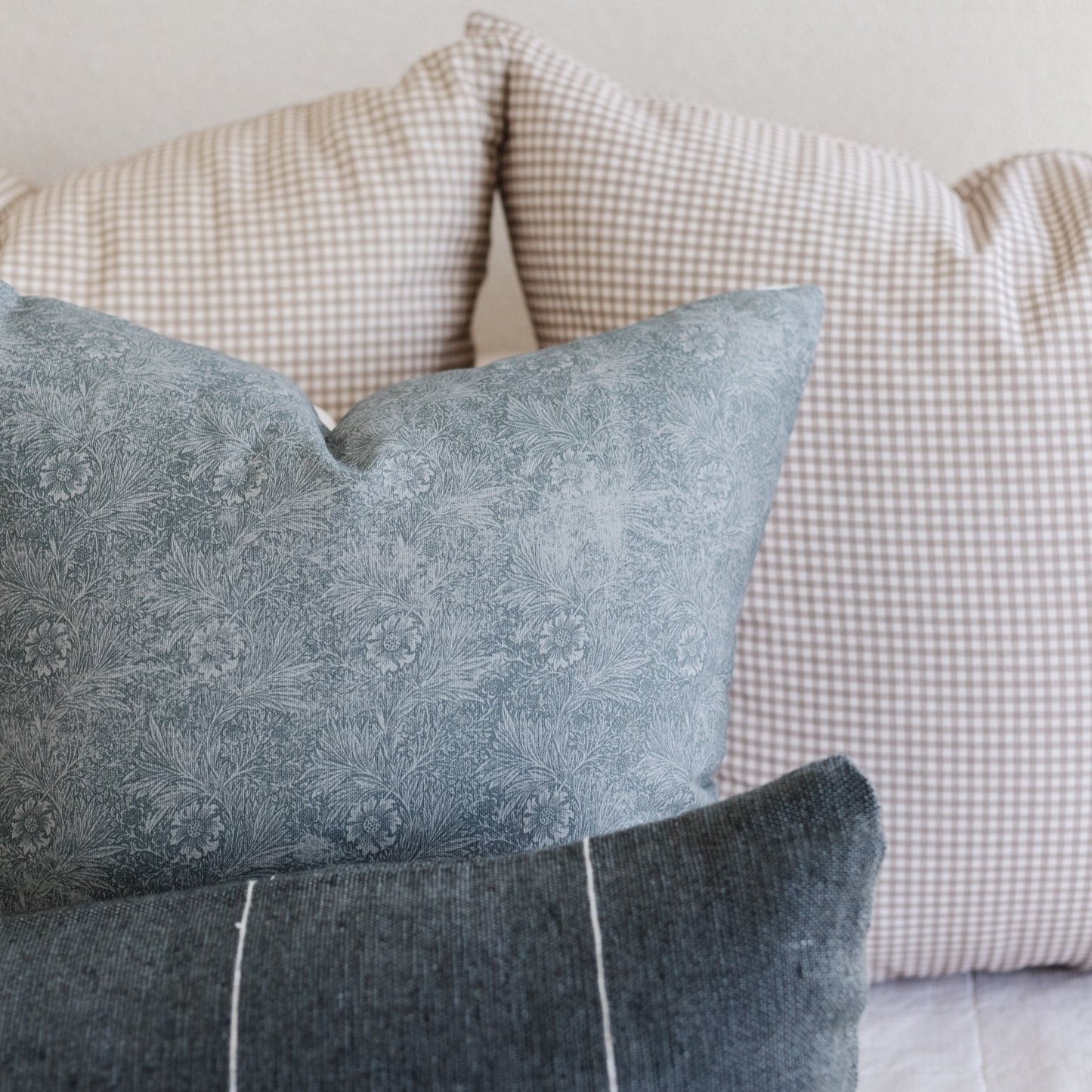 Three decorative pillows with gray floral print, gray textured solid, and beige gingham check patterns stacked together.