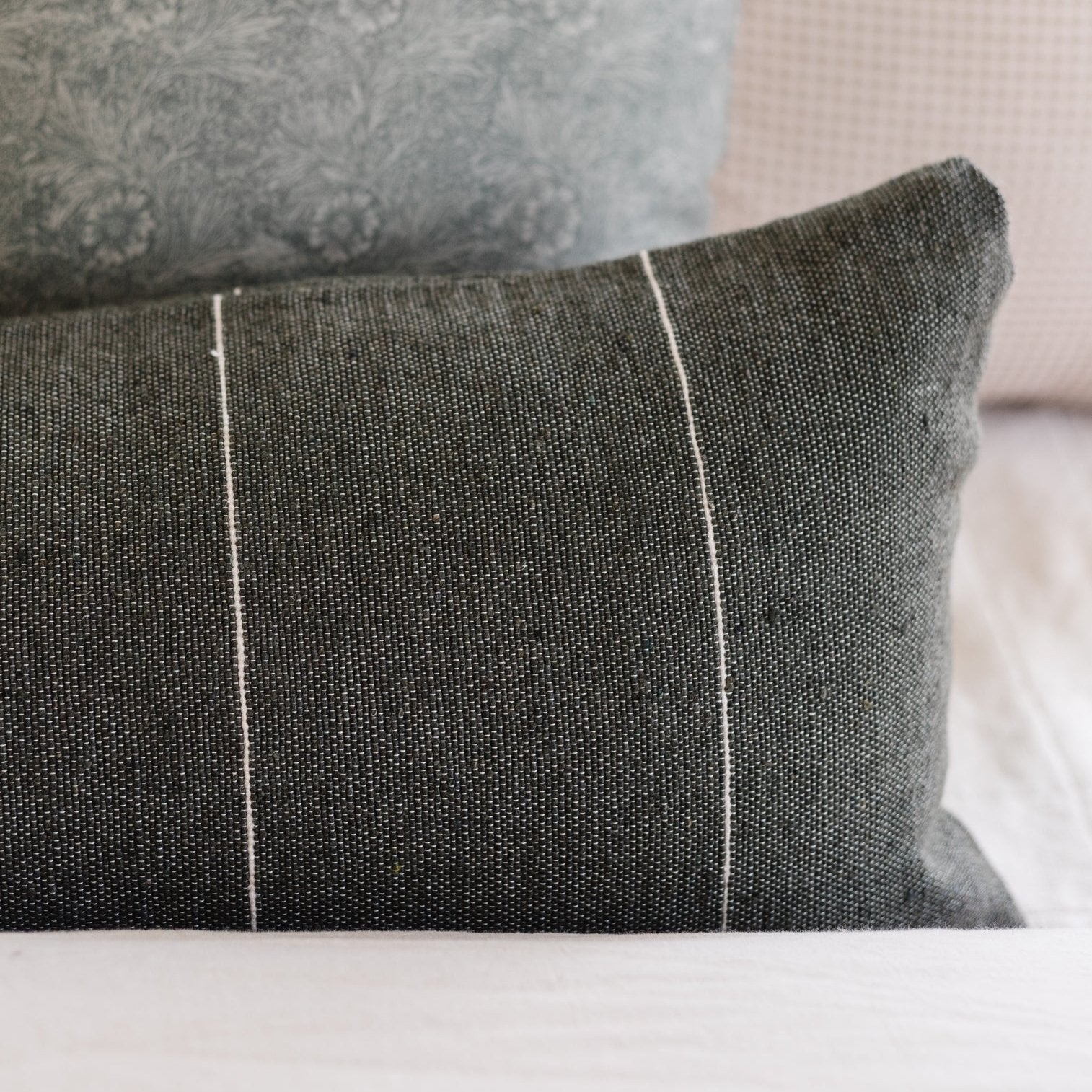 Moss-colored pillow with white piping detail and textured linen weave fabric, paired with patterned throw pillow.