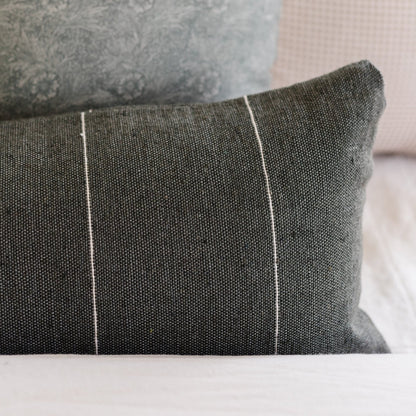 Moss-colored pillow with white piping detail and textured linen weave fabric, paired with patterned throw pillow.