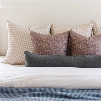 Beige gingham, taupe patterned, and gray lumbar pillows arranged on a white bed with blue checkered bedding.