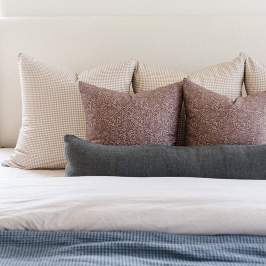 Beige gingham, taupe patterned, and gray lumbar pillows arranged on a white bed with blue checkered bedding.