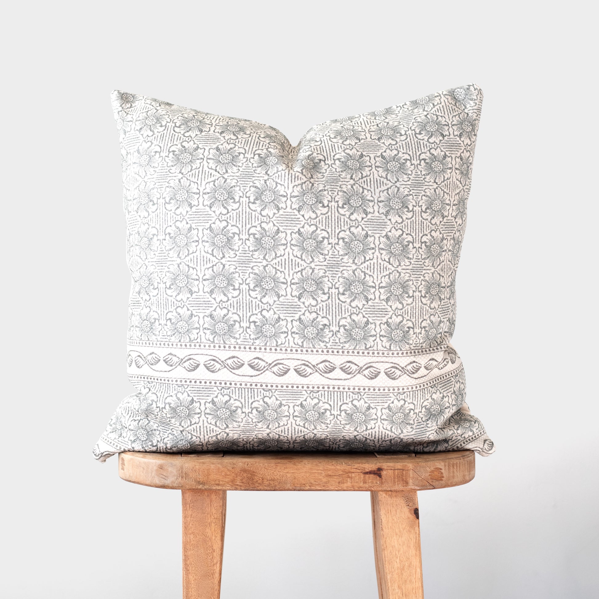 Cream and taupe patterned pillow with geometric and floral design displayed on wooden stool.