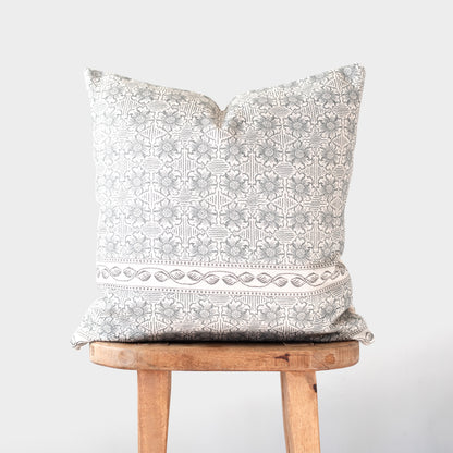 Cream and taupe patterned pillow with geometric and floral design displayed on wooden stool.
