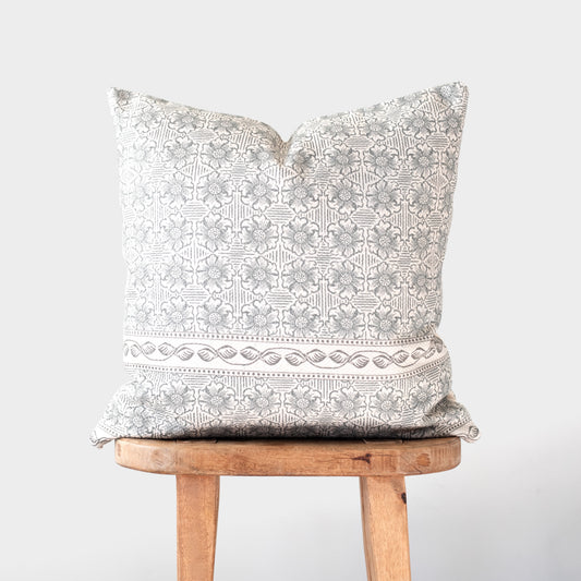 Cream and taupe patterned pillow with geometric and floral design displayed on wooden stool.
