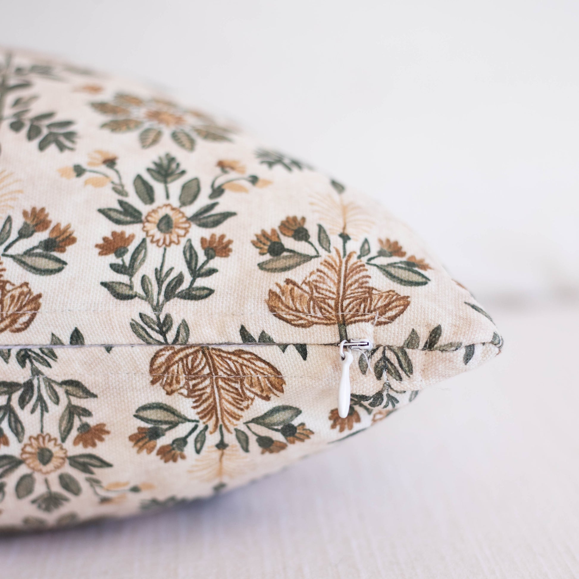 Cream pillow with embroidered botanical pattern in brown, tan, and green featuring flowers and leafy stems with zipper closur