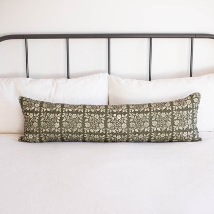 Sage green linen lumbar pillow with white floral leaf pattern on bed with white pillows and metal headboard.