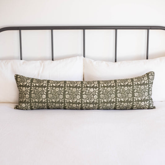 Sage green linen lumbar pillow with white floral leaf pattern on bed with white pillows and metal headboard.