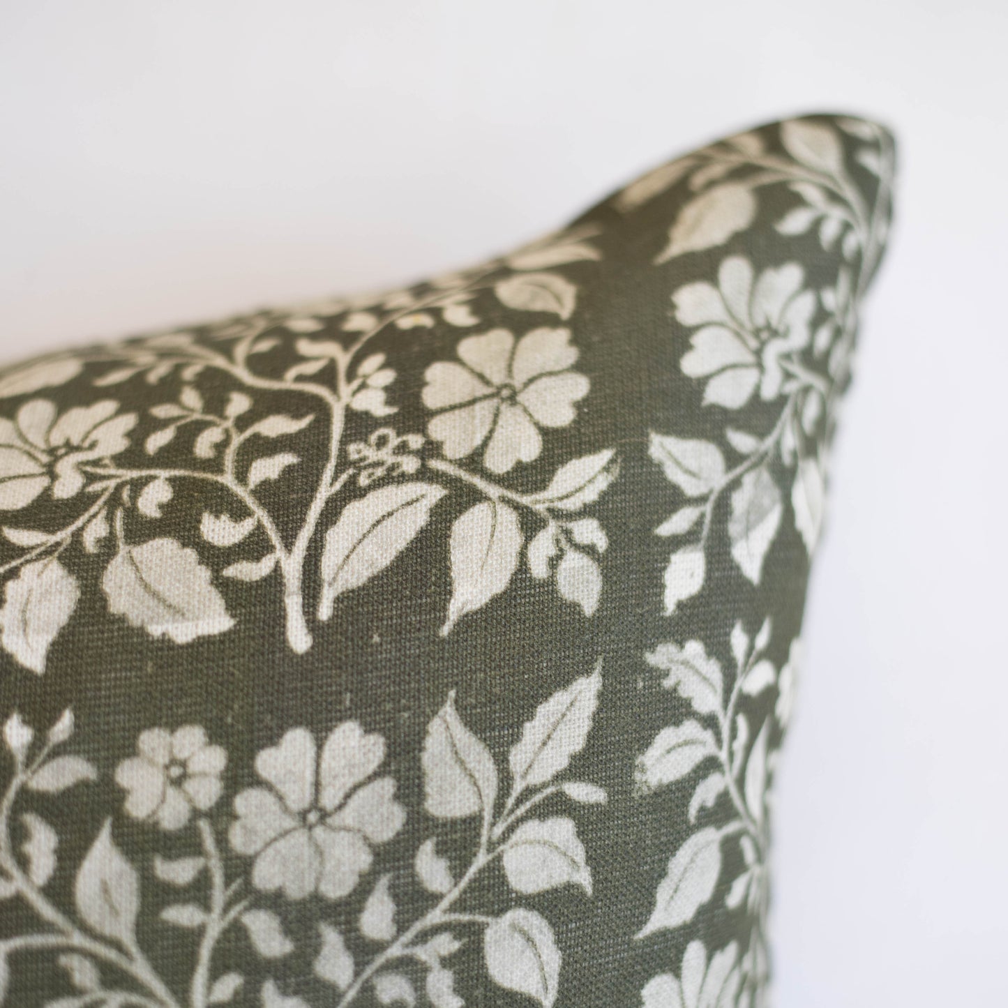 Rectangular lumbar pillow with cream floral pattern on sage green linen fabric.