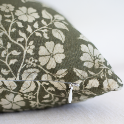 Rectangular lumbar pillow with sage green linen fabric featuring cream floral and leaf pattern, white zipper visible on corne
