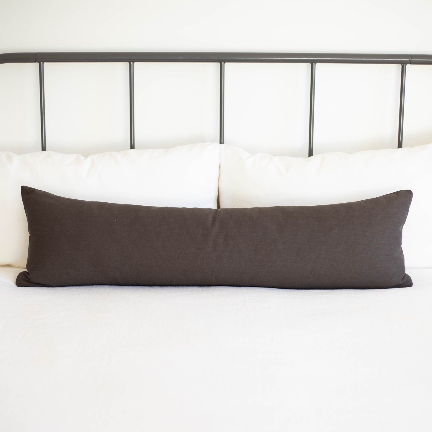 Charcoal gray lumbar pillow displayed horizontally on white bedding against metal headboard.