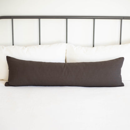 Charcoal gray lumbar pillow displayed horizontally on white bedding against metal headboard.