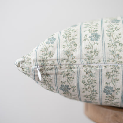 Cream pillow with blue and green floral stripe pattern and white zipper on wooden base.