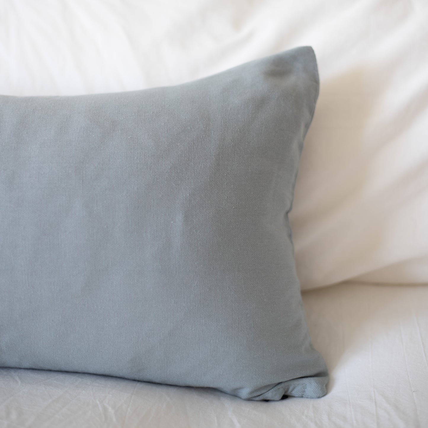 Dusty blue rectangular pillow with solid woven fabric on white bedding.