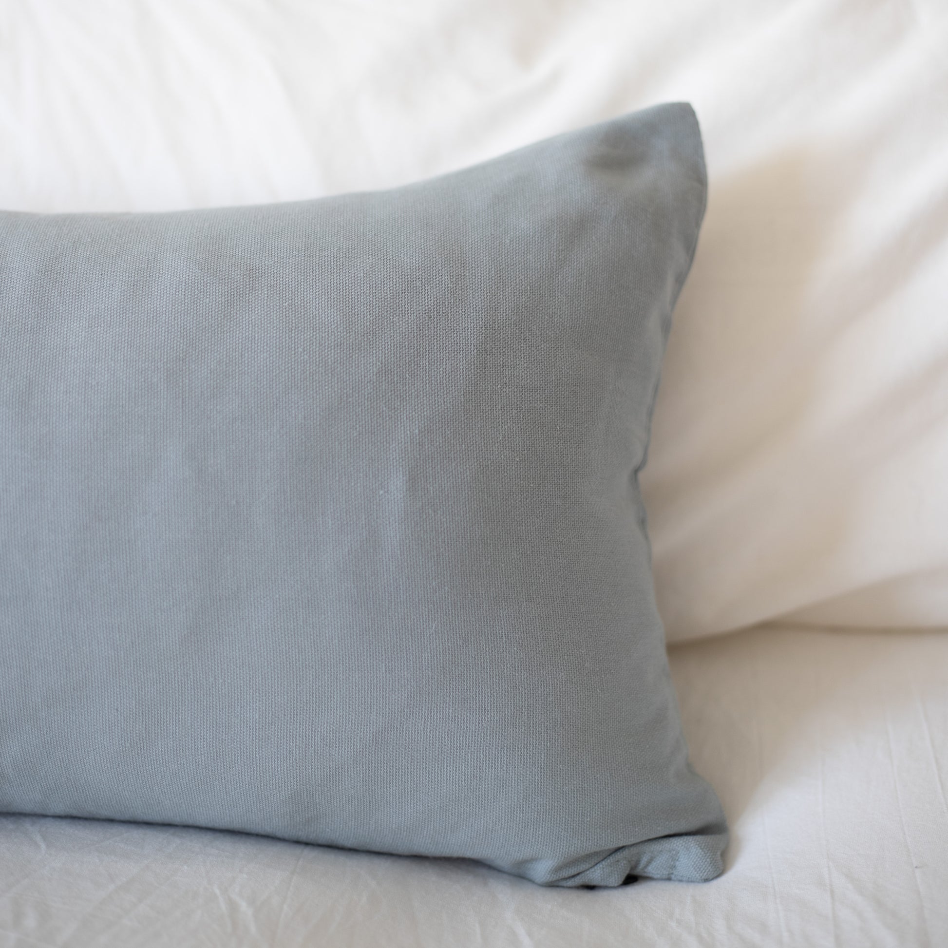 Dusty blue rectangular pillow with solid woven fabric on white bedding.