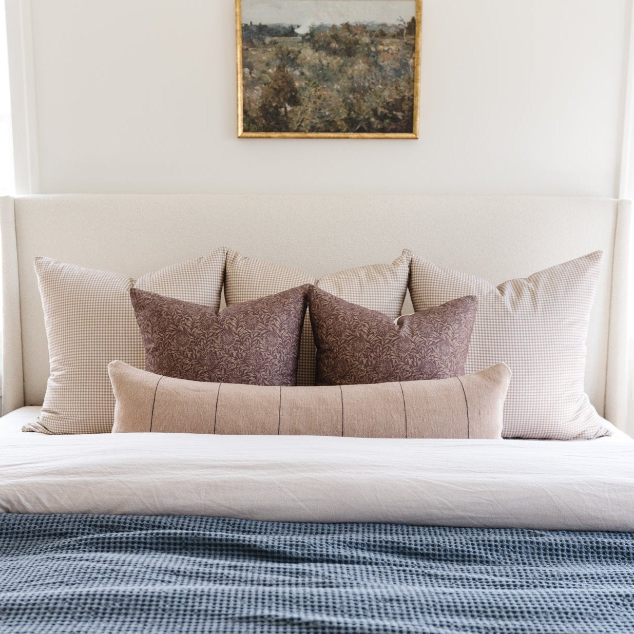Bed with cream upholstered headboard styled with decorative pillows in neutral and brown tones.