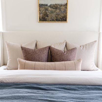 Bed with cream upholstered headboard styled with decorative pillows in neutral and brown tones.