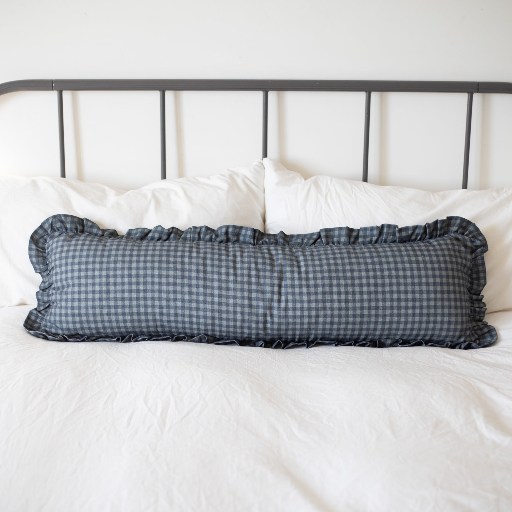 Navy gingham check lumbar pillow with ruffled edges on white bedding.