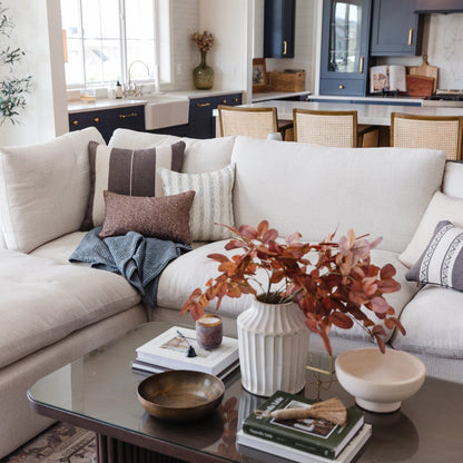Beige upholstered sofa with multiple throw pillows in neutral tones, styled in a modern living room setting.