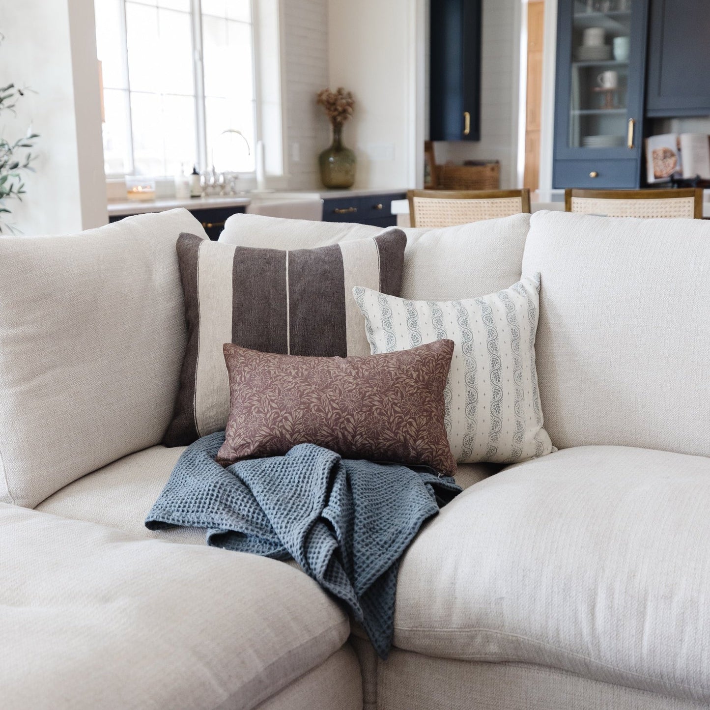 Brown patterned lumbar pillow with white stripe accent displayed on cream sofa with other decorative pillows.