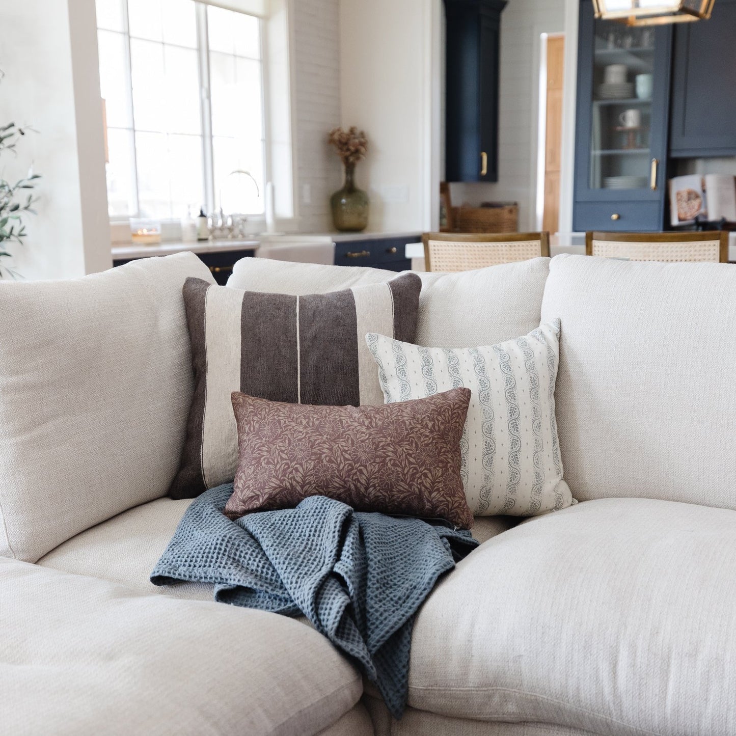 Cream upholstered sofa with gray striped, patterned, and textured throw pillows and blue knit blanket.