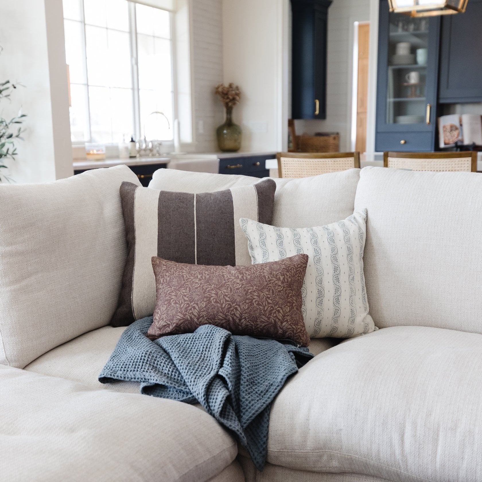 Cream upholstered sofa with gray striped, patterned, and textured throw pillows and blue knit blanket.