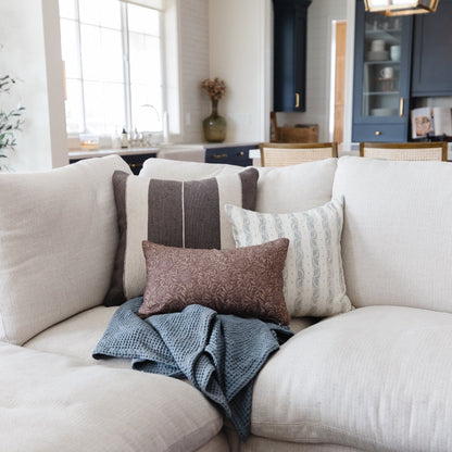 Cream upholstered sofa with gray striped, patterned, and textured throw pillows and blue knit blanket.