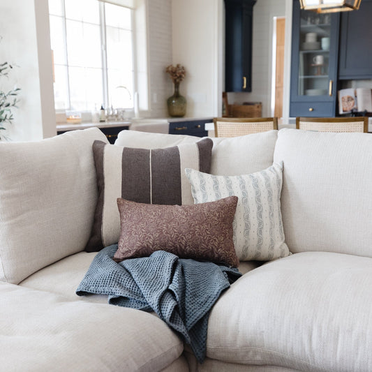 Cream upholstered sofa with gray striped, patterned, and textured throw pillows and blue knit blanket.