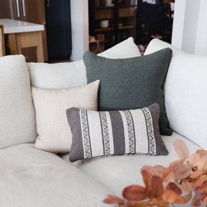 Gray and cream lumbar pillow with striped pattern and geometric detailing, displayed among coordinating pillows on a light so