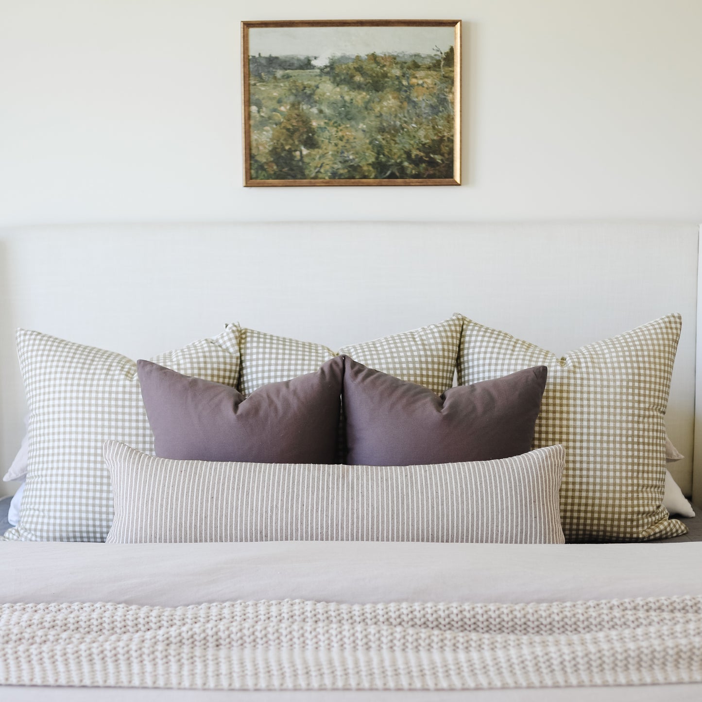 Tan lumbar pillow with vertical striped pattern displayed on bed between checkered accent pillows.