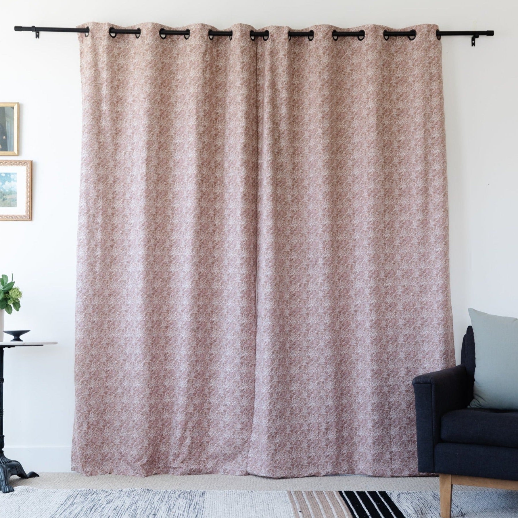Two mauve textured curtain panels with grommet top rings hanging on a black rod over a window.
