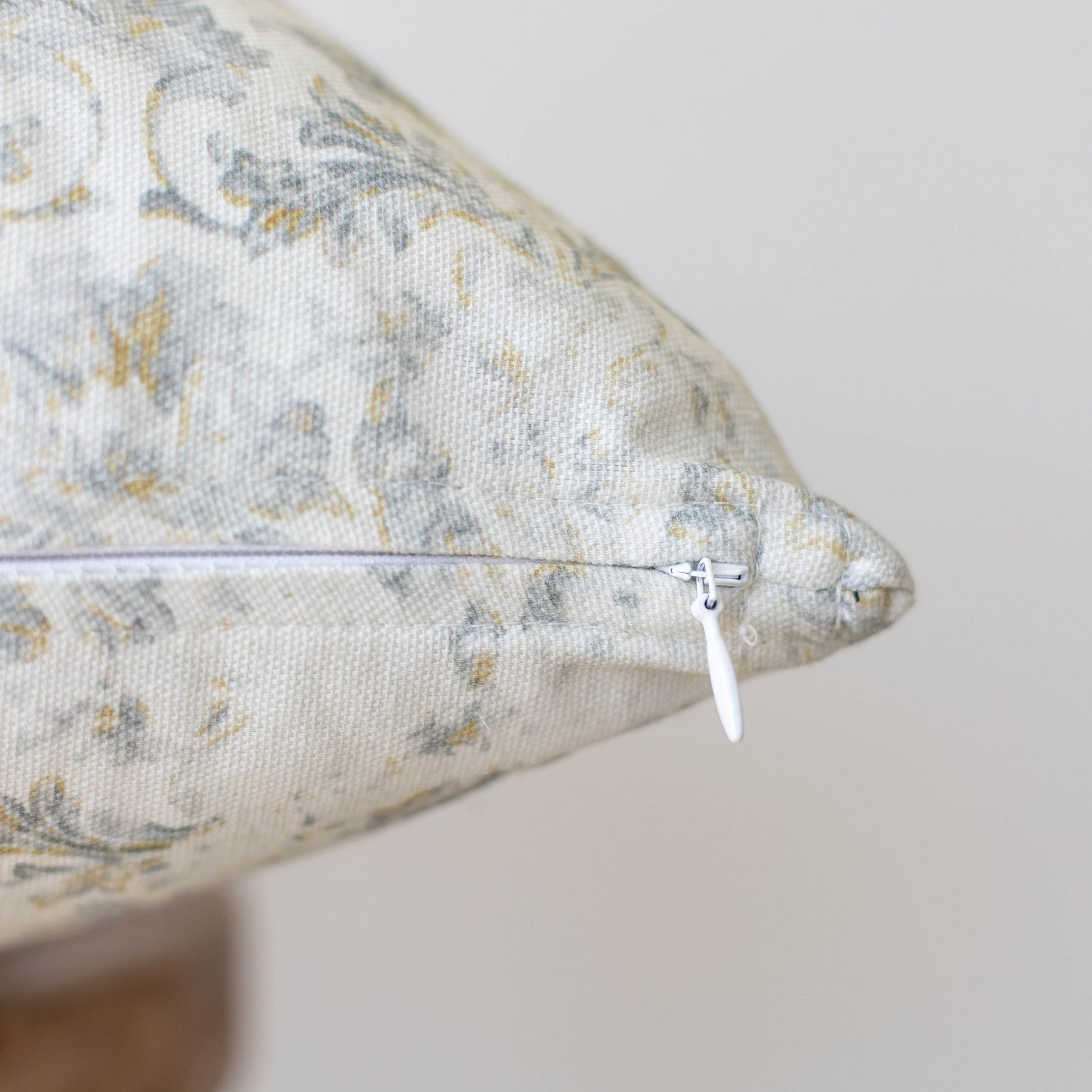 Cream linen pillow with gray and gold floral pattern and white zipper closure.