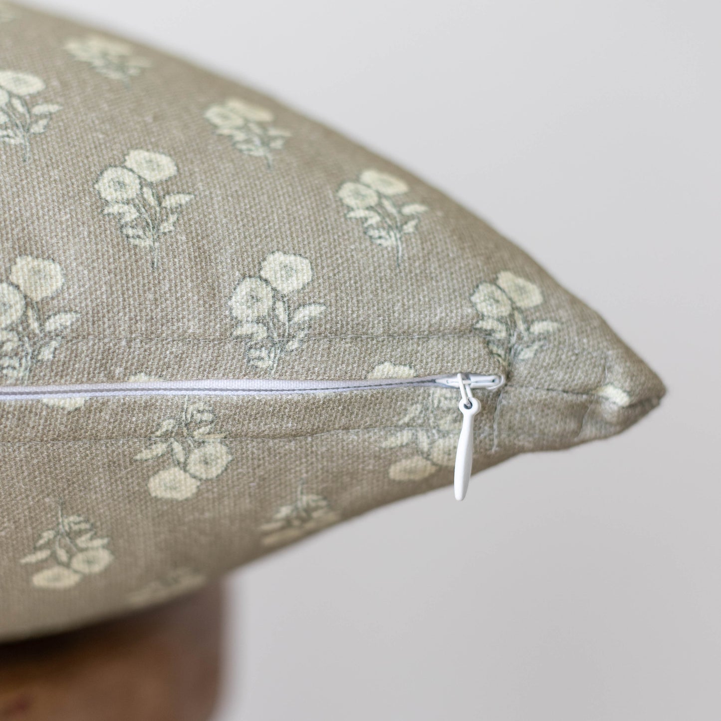 Beige linen pillow with cream floral print and white zipper closure.