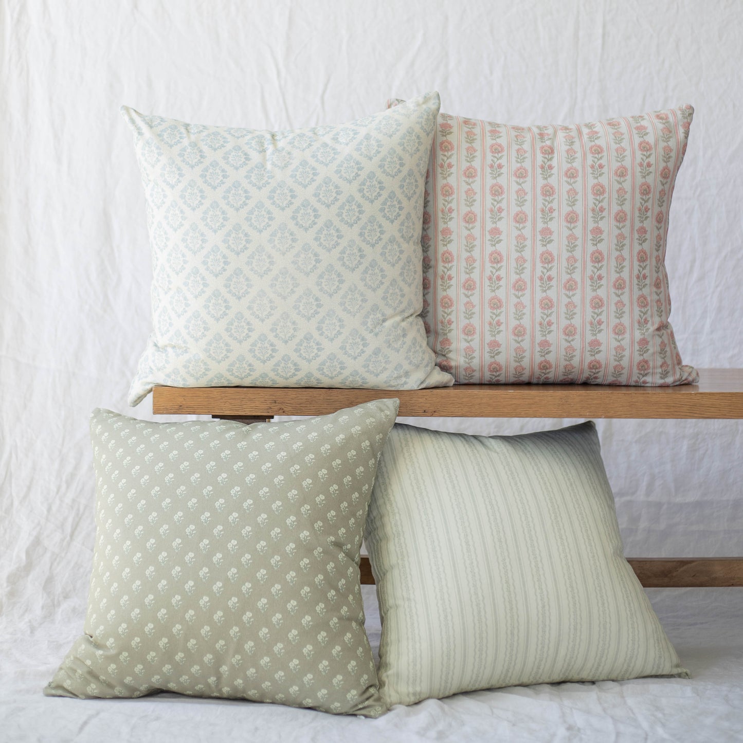 Four decorative pillows in coordinating patterns: blue diamond, coral floral stripe, sage dotted, and cream ribbed designs.
