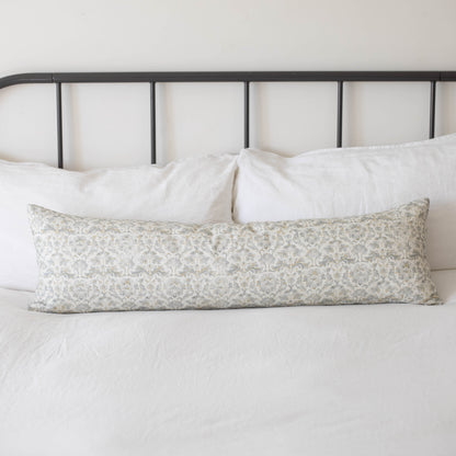 Long rectangular throw pillow with beige floral pattern resting on white bedding against black metal headboard.