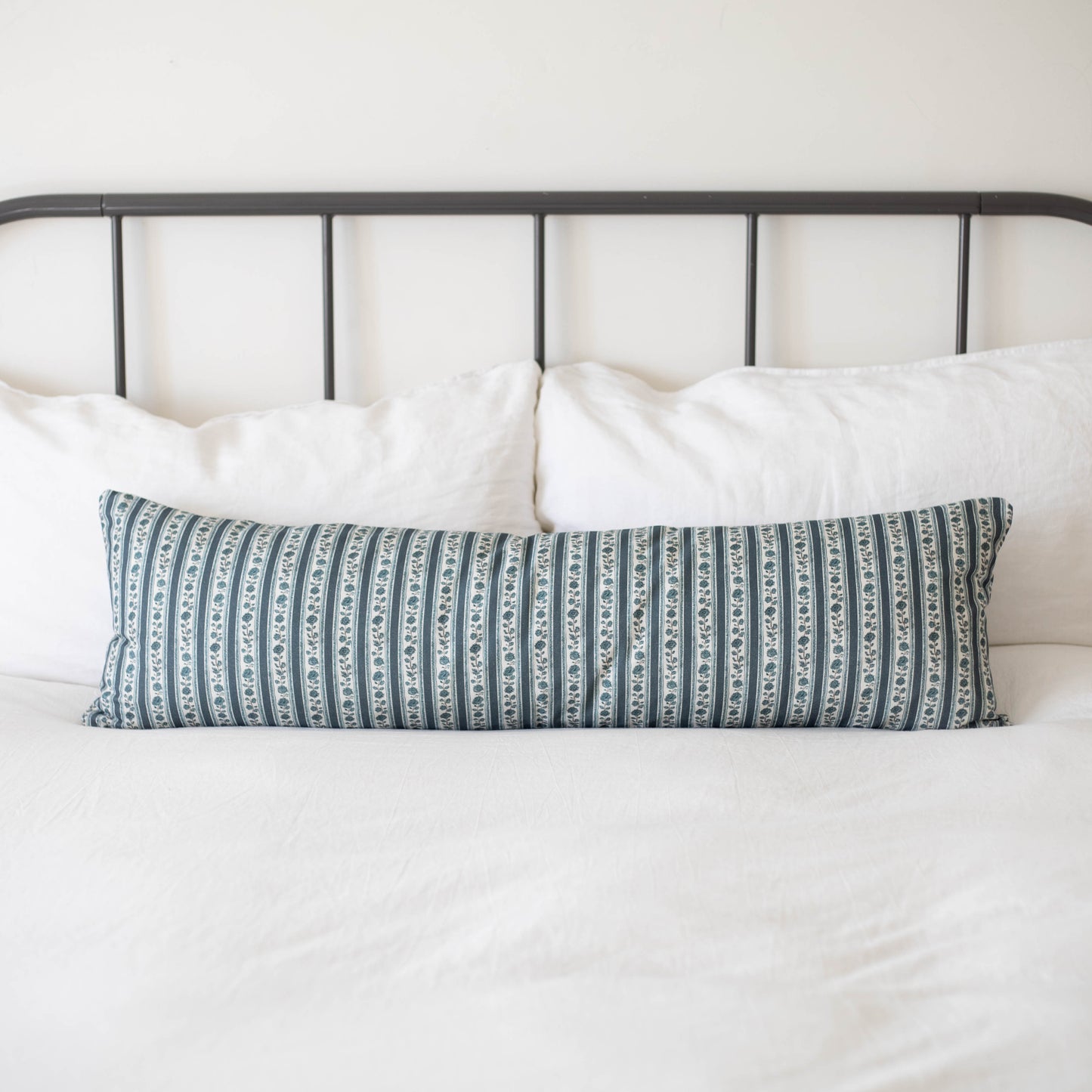 Beau blue and white striped lumbar pillow on bed with white pillows and metal headboard.