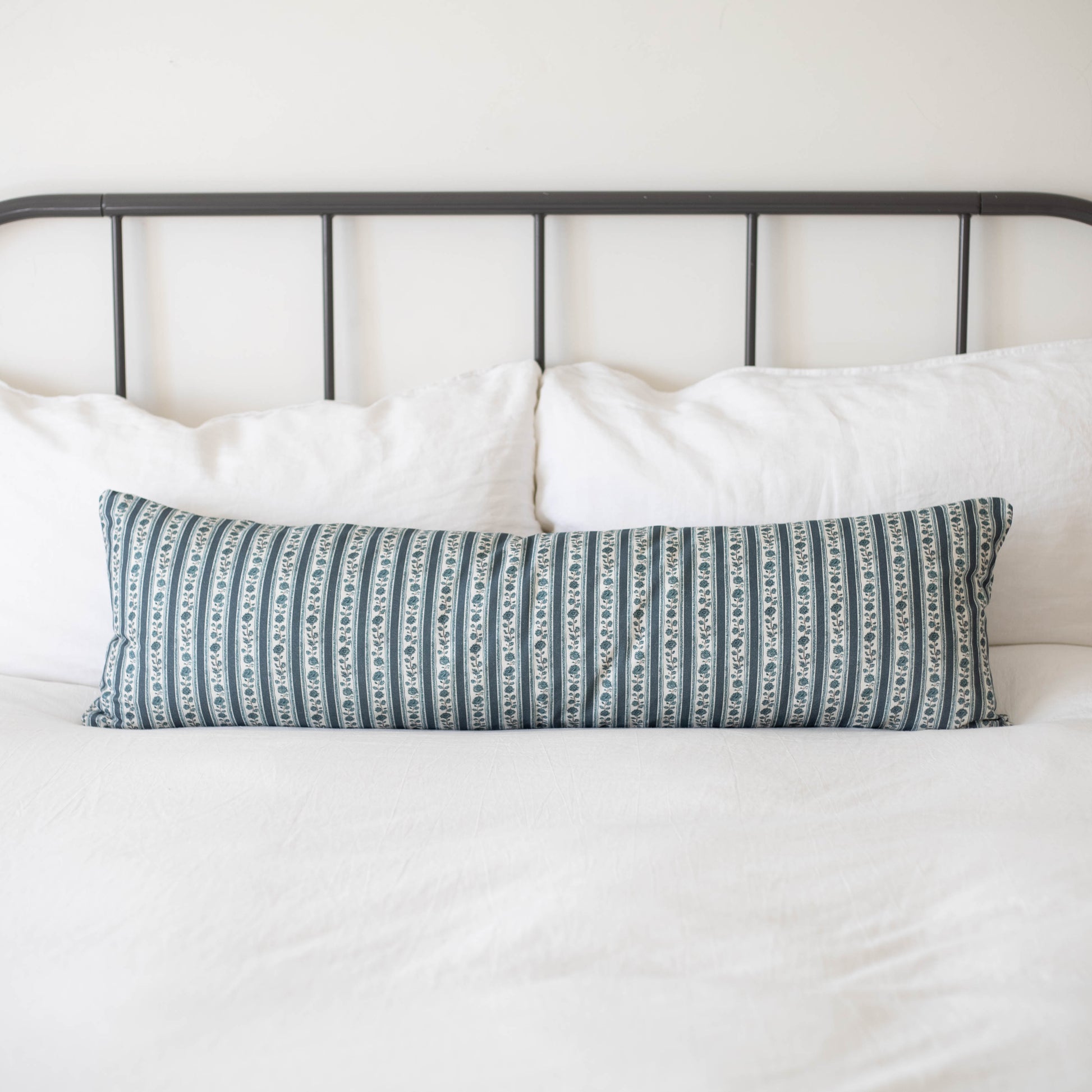 Beau blue and white striped lumbar pillow on bed with white pillows and metal headboard.