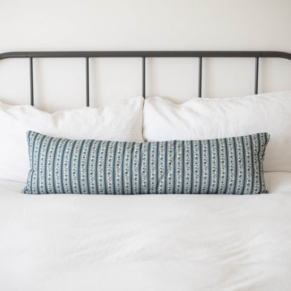 Beau blue and white striped lumbar pillow on bed with white pillows and metal headboard.