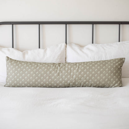 Sage green lumbar pillow with small white floral pattern on bed with white pillows and metal headboard.