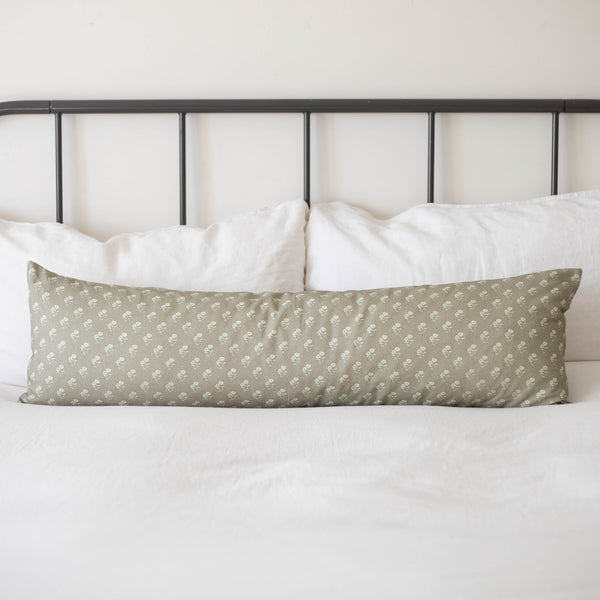 Sage green lumbar pillow with small white floral pattern on bed with white pillows and metal headboard.