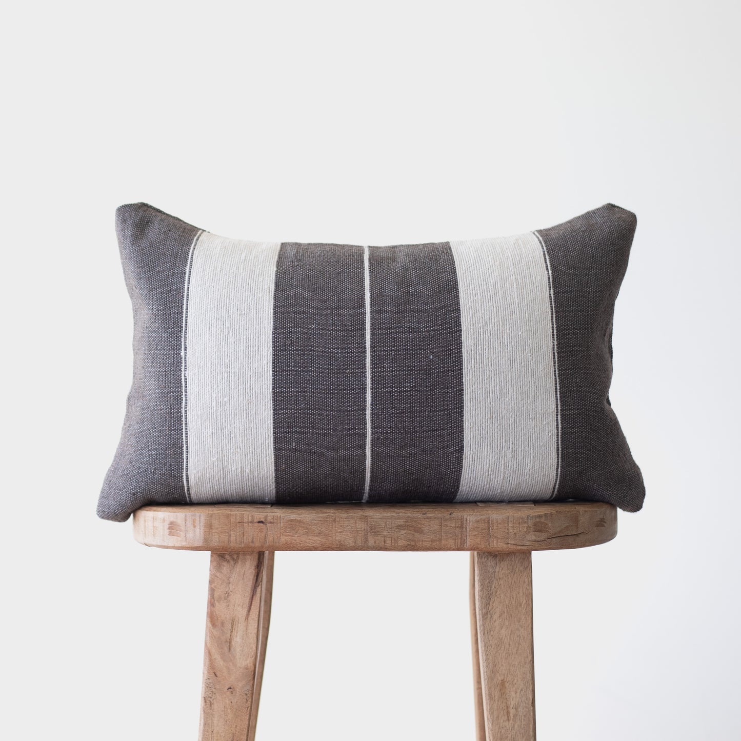 Charcoal and cream striped lumbar pillow with vertical bands displayed on a wooden stool.