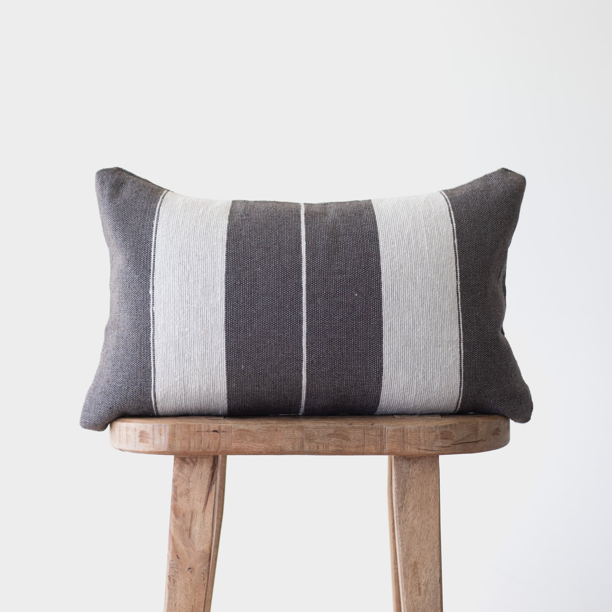 Charcoal and cream striped lumbar pillow with vertical bands displayed on a wooden stool.