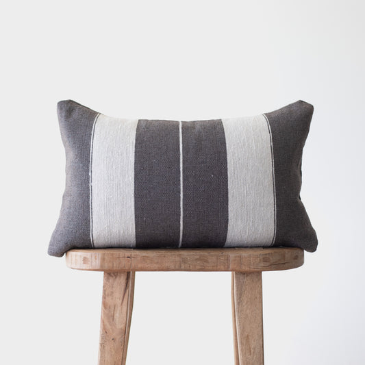 Charcoal and cream striped lumbar pillow with vertical bands displayed on a wooden stool.