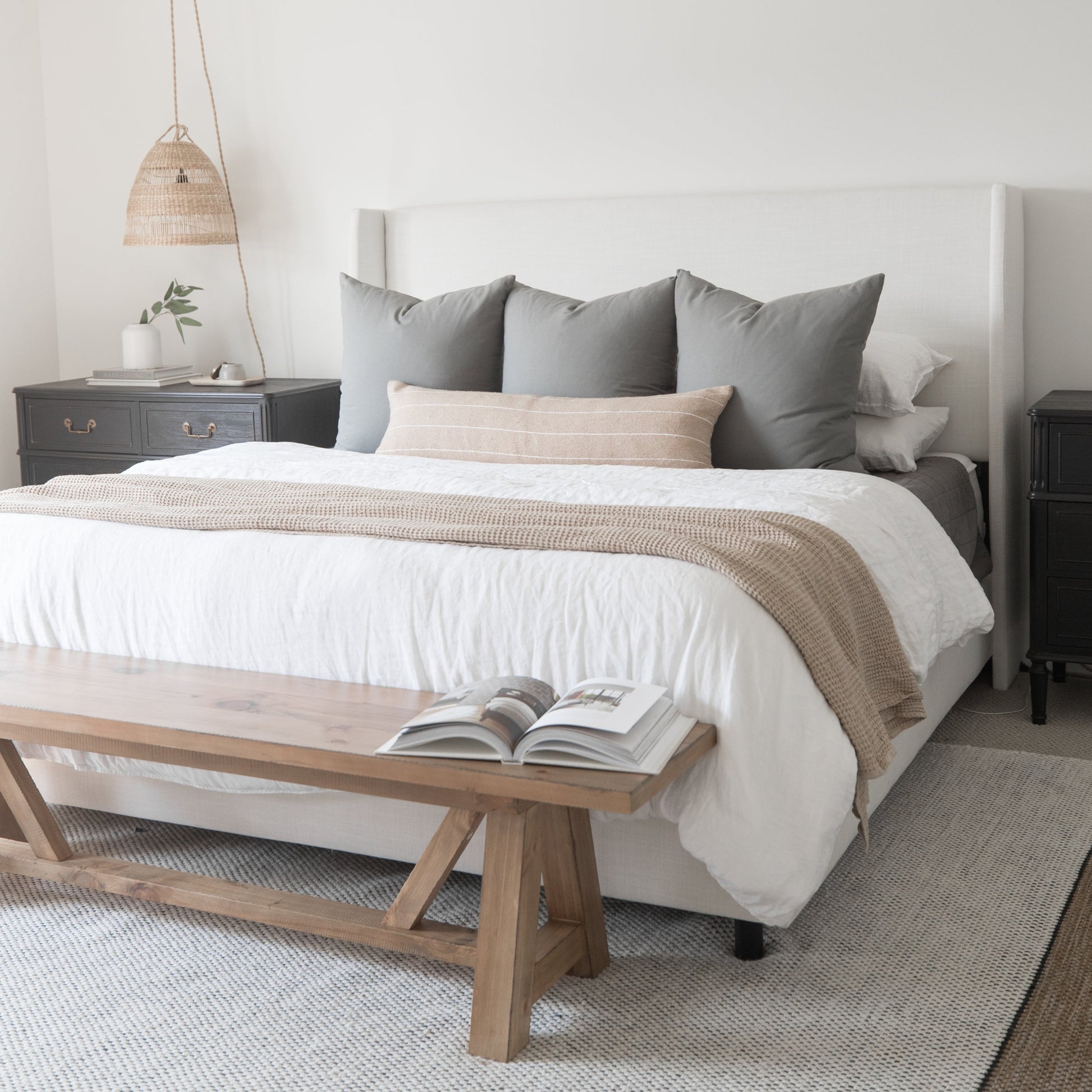 Beige and gray pillows arranged on white bedding with tan striped throw in bedroom setting.
