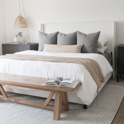 Beige and gray pillows arranged on white bedding with tan striped throw in bedroom setting.