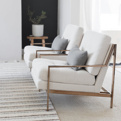 Two cream upholstered armchairs with gray cushions and wooden frames arranged in a living room setting.